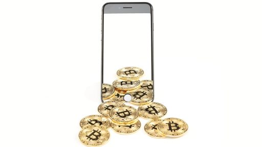 Fysieke bitcoin munten liggend op een bureau naast een laptop met koersgrafiek