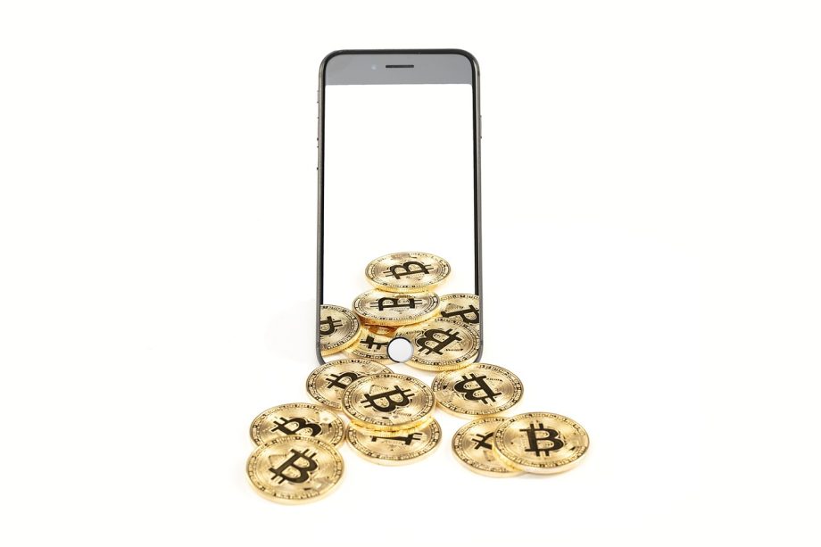 Fysieke bitcoin munten liggend op een bureau naast een laptop met koersgrafiek