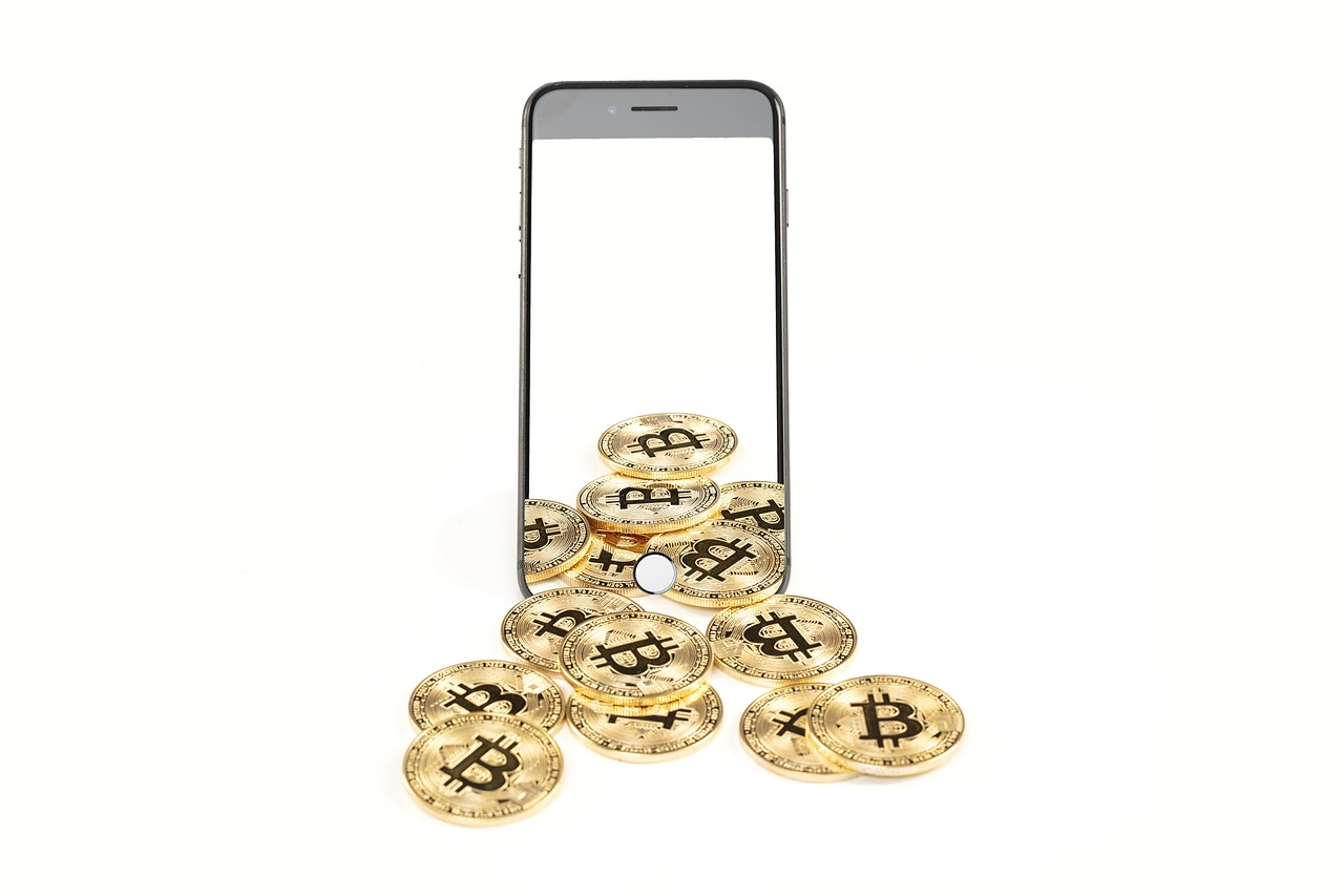 Fysieke bitcoin munten liggend op een bureau naast een laptop met koersgrafiek